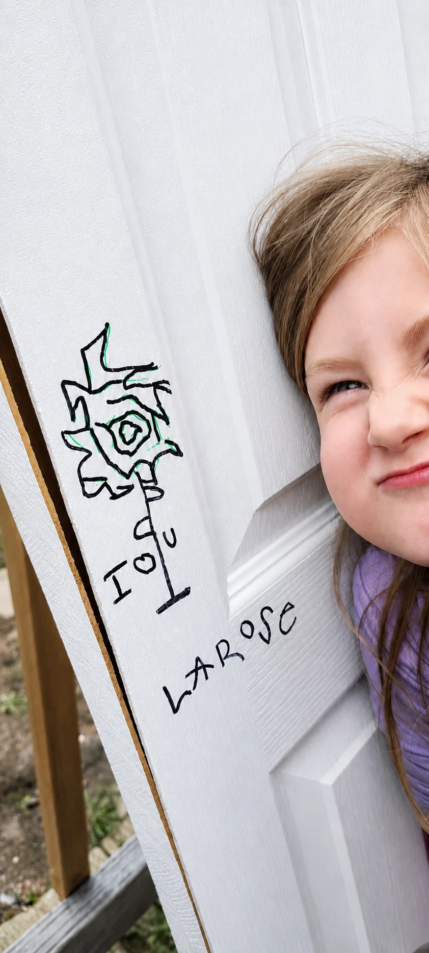 Emma Rose près de son dessin de rose et de sa signature manuscrite LAROSE sur une porte blanche.